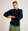 A blonde-haired woman wears the Ailsa Navy Knitted Cardigan and a green skirt, standing against a plain light background with one arm folded over the other.