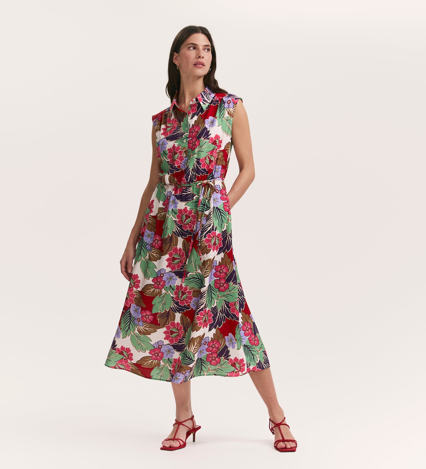 A woman in the Alida Red Floral Sleeveless Midi Dress stands against a plain light background, styled with red heeled sandals.