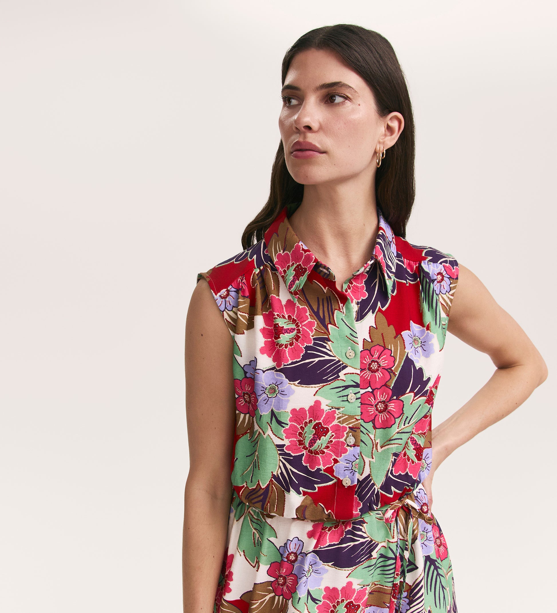 A woman with long dark hair models the Alida Red Floral Sleeveless Midi Dress, featuring vibrant red, pink, green, and purple hues, against a plain light background.