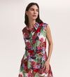 A woman wears the Alida Red Floral Sleeveless Midi Dress featuring a collared neckline and vibrant floral print. She stands against a plain background, looking to the side with one hand in her pocket.