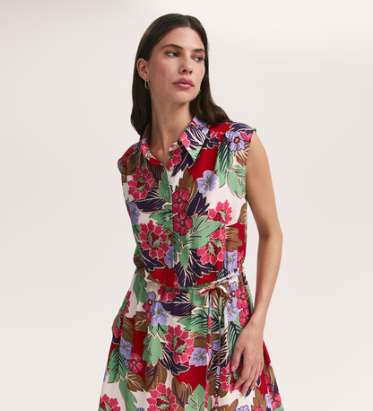 A woman wears the Alida Red Floral Sleeveless Midi Dress featuring a collared neckline and vibrant floral print. She stands against a plain background, looking to the side with one hand in her pocket.