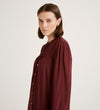 A woman with straight brown hair wears the Beccy Burgundy Crepe Short Dress, standing against a plain light background and looking slightly to the side.