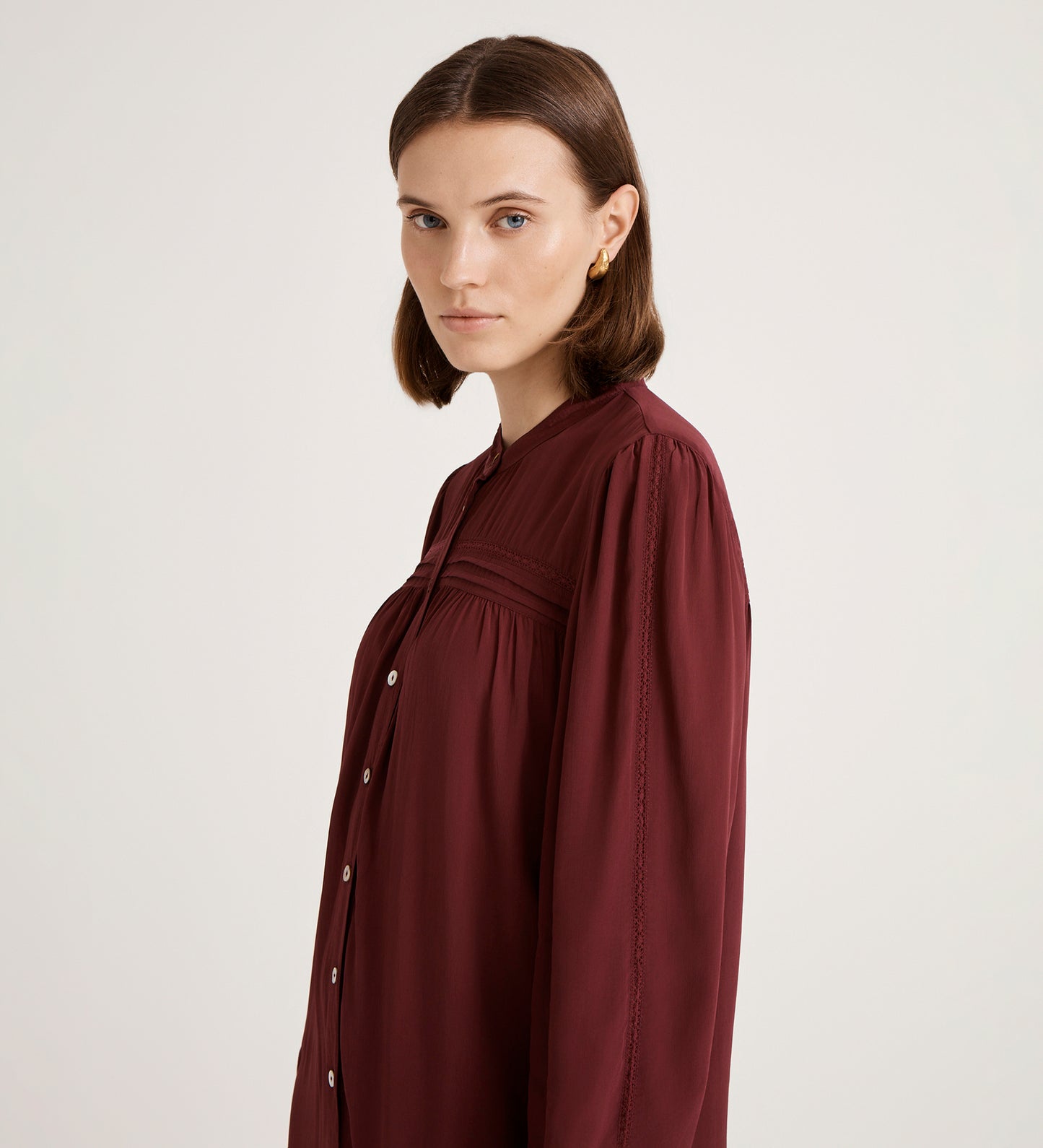 A woman with straight brown hair wears the Beccy Burgundy Crepe Short Dress, standing against a plain light background and looking slightly to the side.