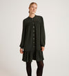 A woman wears the Beccy Forest Green Crepe Short Dress, featuring long sleeves, a loose fit, mandarin collar, button-down front, and ruffled hem, standing against a plain light background.