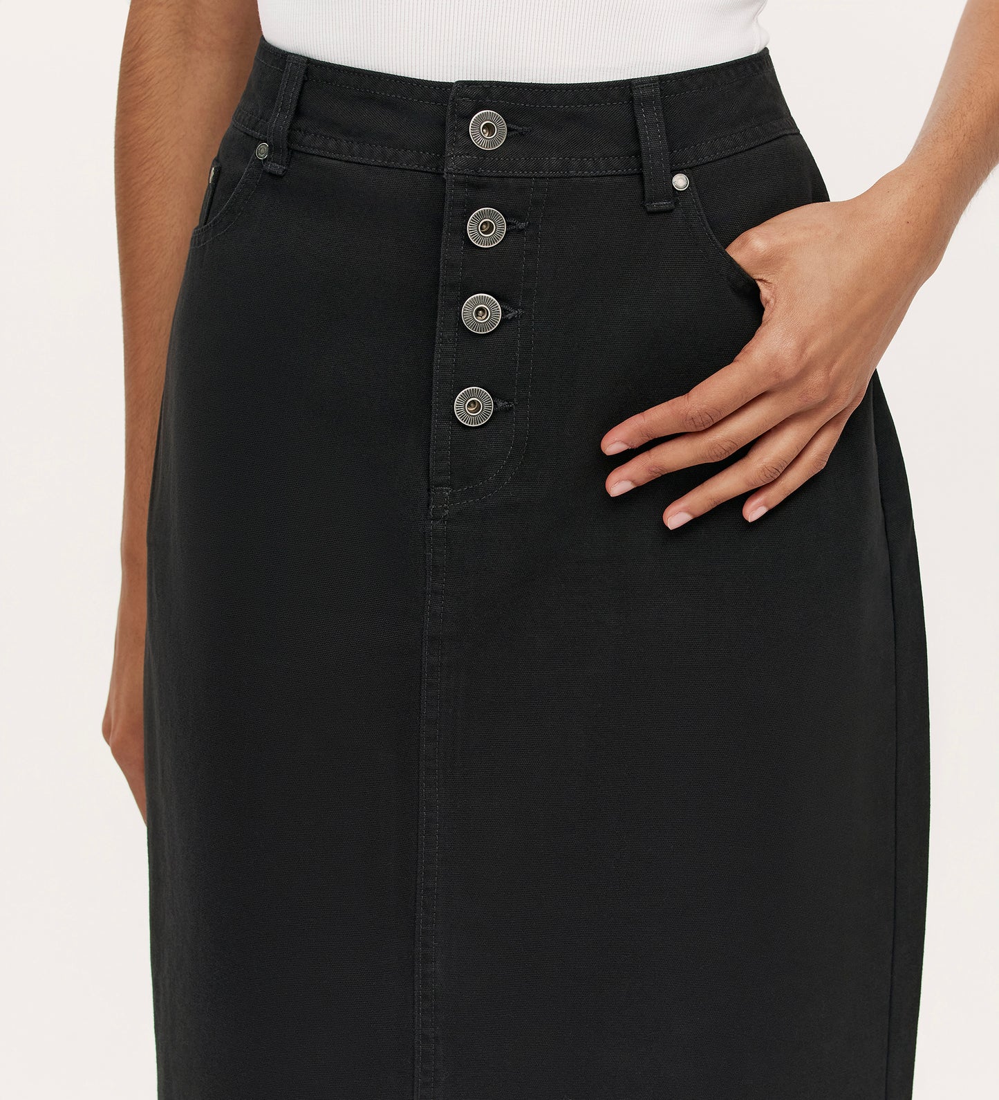 Close-up of a person wearing the Beth Black Canvas Midi Skirt, featuring a high waistband, four front buttons, a side pocket with one hand in it, paired with a white top.
