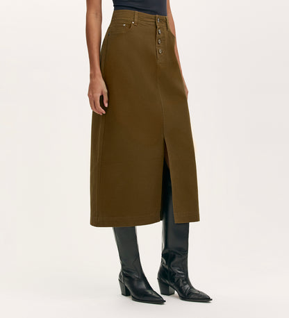Wearing the Beth Khaki Canvas Midi Skirt featuring a high waistband, button front, and front slit, paired with black knee-high boots and a sleeveless top, a person stands against a plain light background.