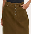 A person wearing the Beth Khaki Canvas Midi Skirt, a high-waisted olive green skirt with front button closure, their right hand in the pocket. The top of the midi-length skirt and part of a black shirt are visible.