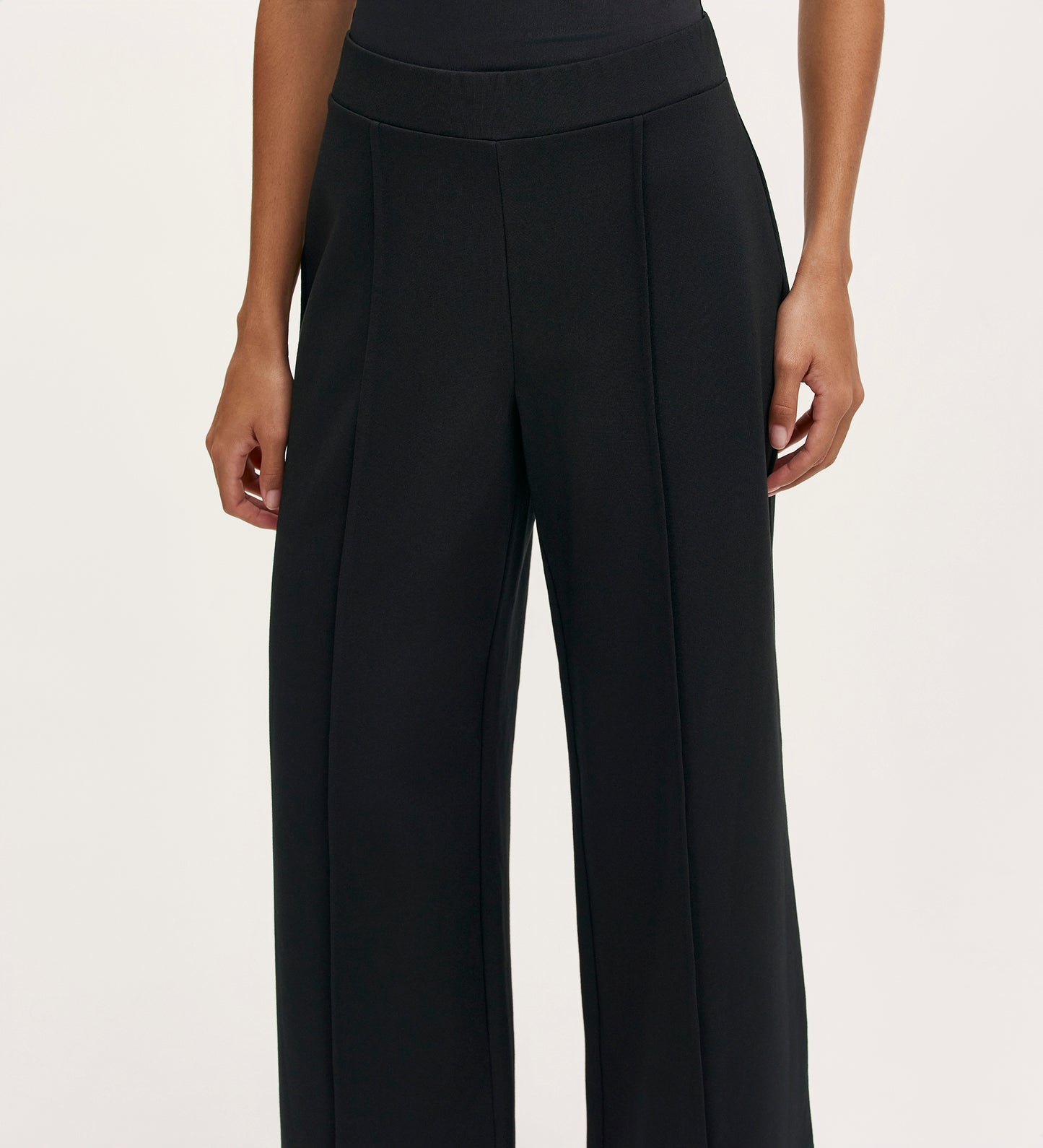 A woman wearing the Caryl Black Ponte Jersey Wide Leg Trouser, featuring pintuck detailing and an elasticated waistband.
