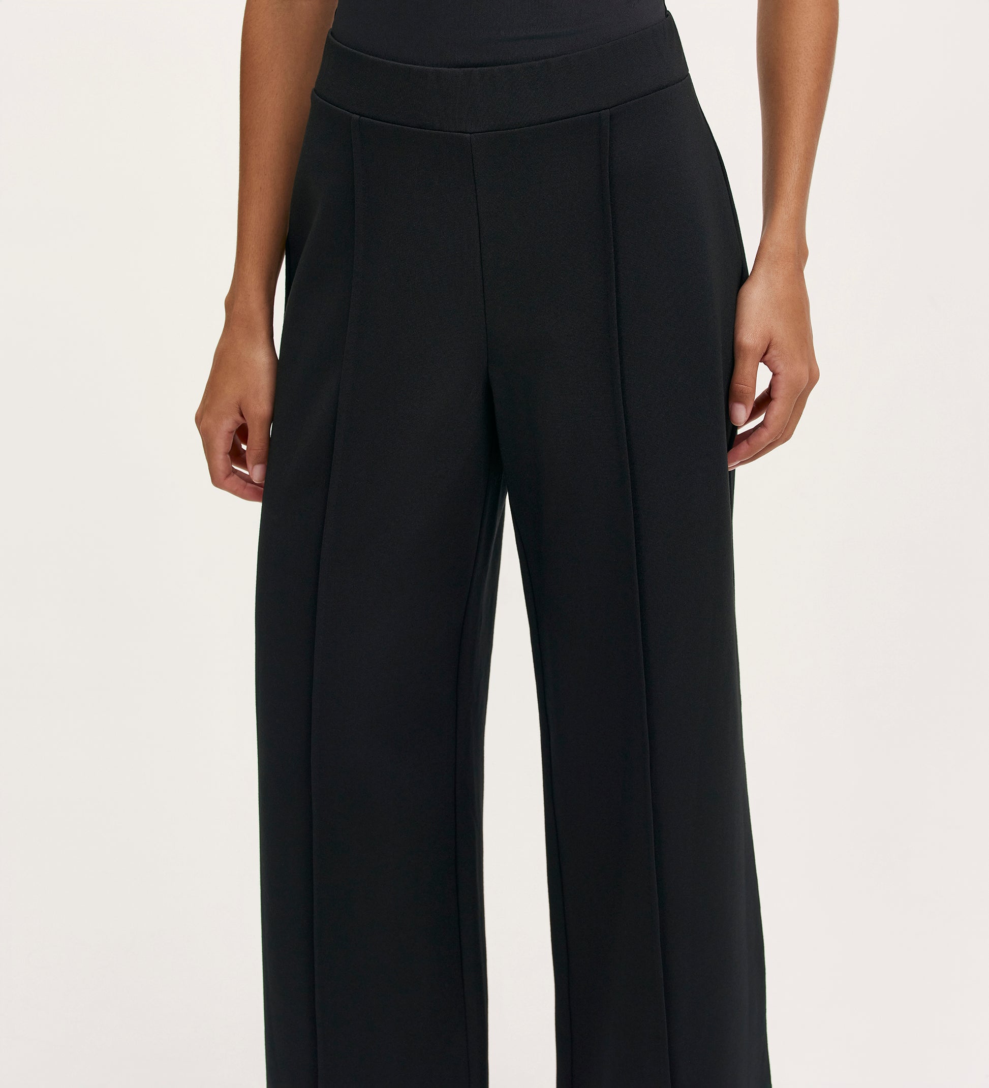 A woman wearing the Caryl Black Ponte Jersey Wide Leg Trouser, featuring pintuck detailing and an elasticated waistband.