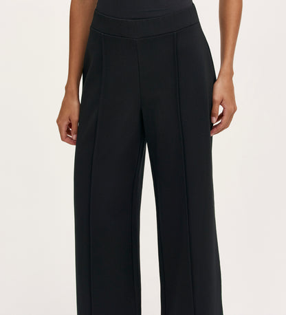 A woman wearing the Caryl Black Ponte Jersey Wide Leg Trouser, featuring pintuck detailing and an elasticated waistband.
