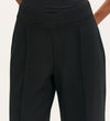 A close-up of a person wearing the Caryl Black Ponte Jersey Wide Leg Trouser and a black top, with arms slightly behind their back. The image highlights the waist and upper legs of the tailored, high-waisted pants.