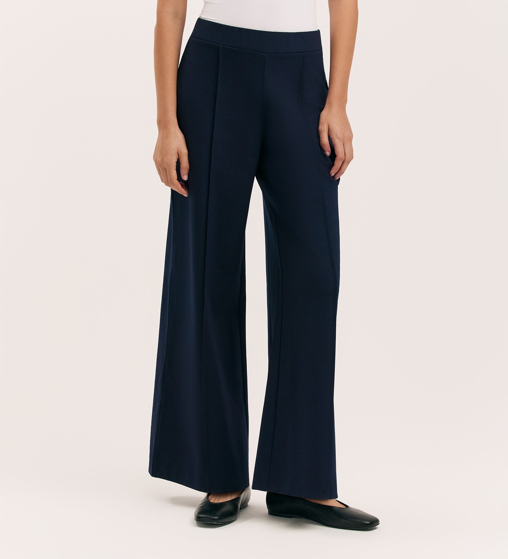 Someone is wearing Caryl Navy Ponte Jersey Wide Leg Trousers with an elasticated waistband, a white top, and black flats. The cropped image captures only the lower torso and legs against a plain light background.