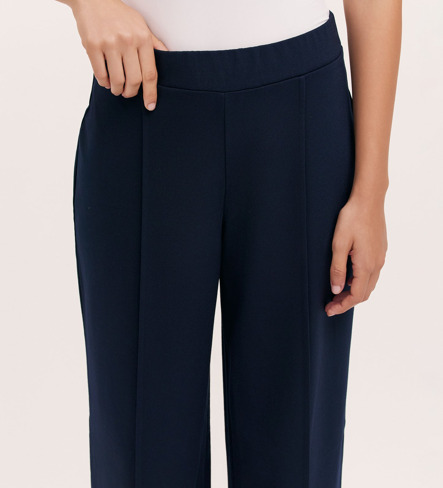 A person wears the Caryl Navy Ponte Jersey Wide Leg Trouser with an elasticated waistband and a white top, shown from waist to mid-thigh. One hand rests on the waistband while the other hangs by their side.