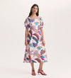 A woman wears the Daisy Cream Leaves Crepe Midi Dress with colorful floral patterns, puffed short sleeves, and a square neckline. She stands against a light background and pairs it with red strappy high-heeled sandals.