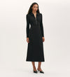 A woman stands against a plain background wearing the Elvira Black Jersey Midi Dress with long sleeves, a front zip, collared neckline, and black heels.
