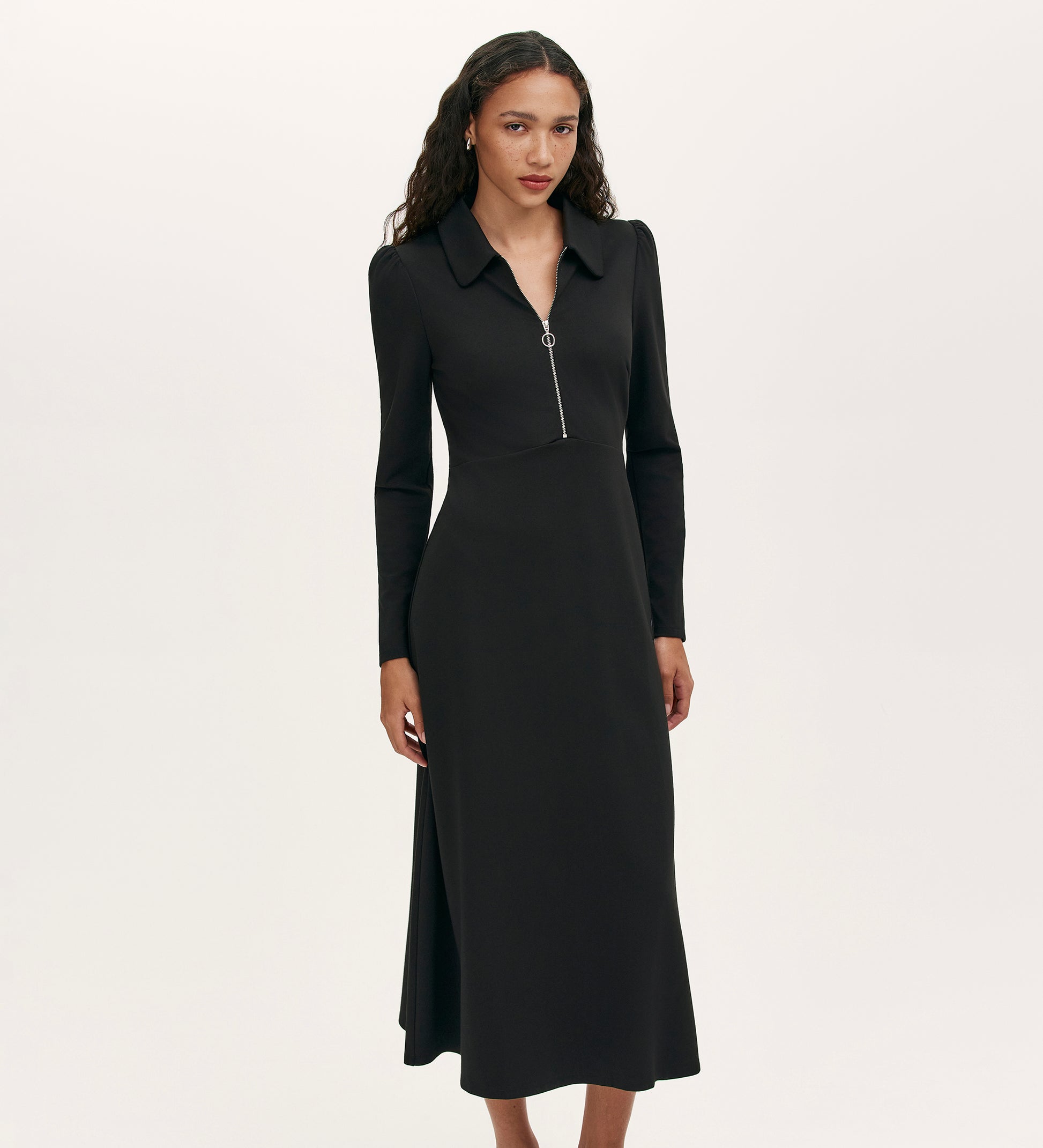 A woman wearing the Elvira Black Jersey Midi Dress, featuring a collared neckline, long sleeves, and a front zip, stands against a plain white background.
