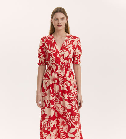 A woman faces forward in the Emily Red Tropical Bloom Midi Dress, featuring a white floral print, short puff sleeves, elastic waist, and v-neckline, set against a plain light background.
