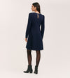 A woman faces away, wearing the Eva Navy Ponte Jersey Short Dress with long sleeves, princess seams, and a back keyhole detail, paired with black tights and ankle boots against a plain light background.