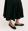 A person models the Fabiola Black Crepe Midi Skirt with black flats, standing against a plain, light background. Only their lower legs and feet are shown.