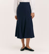 A person wearing a white long-sleeve blouse, the Fabiola Navy Crepe Midi Skirt, and black flat shoes stands against a plain light background.