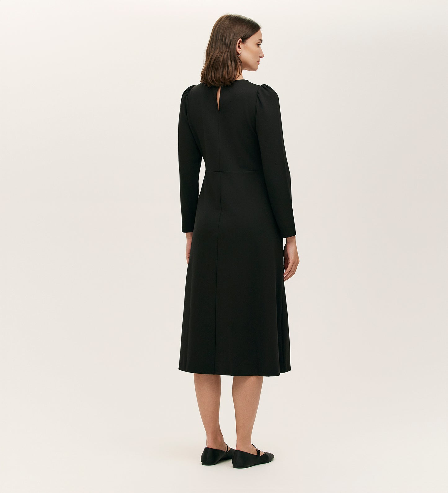 A woman faces away, wearing the Felice Black Ponte Jersey Midi Dress with long sleeves and black flats, set against a plain light background.
