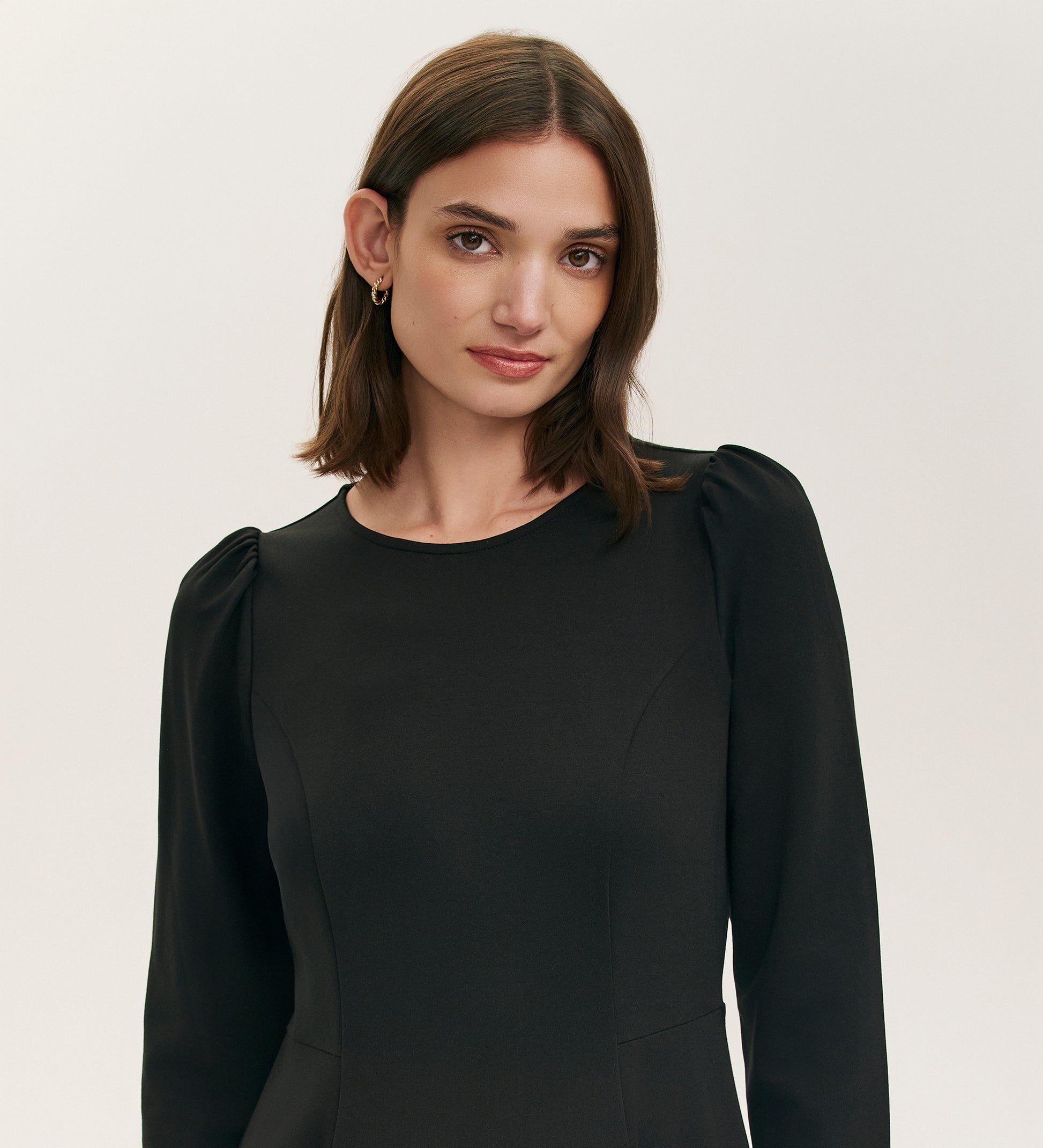 A woman with shoulder-length brown hair wears the Felice Black Ponte Jersey Midi Dress, featuring long sleeves and a tailored fit, standing against a plain light background and looking at the camera with a neutral expression.