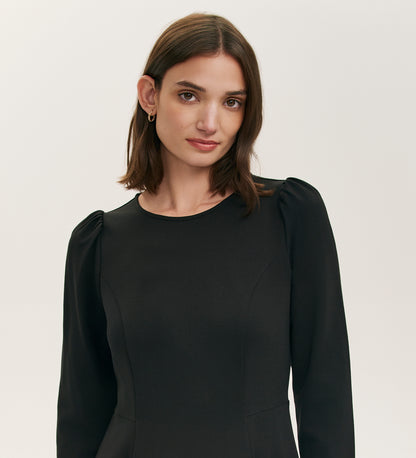 A woman with shoulder-length brown hair wears the Felice Black Ponte Jersey Midi Dress, featuring long sleeves and a tailored fit, standing against a plain light background and looking at the camera with a neutral expression.