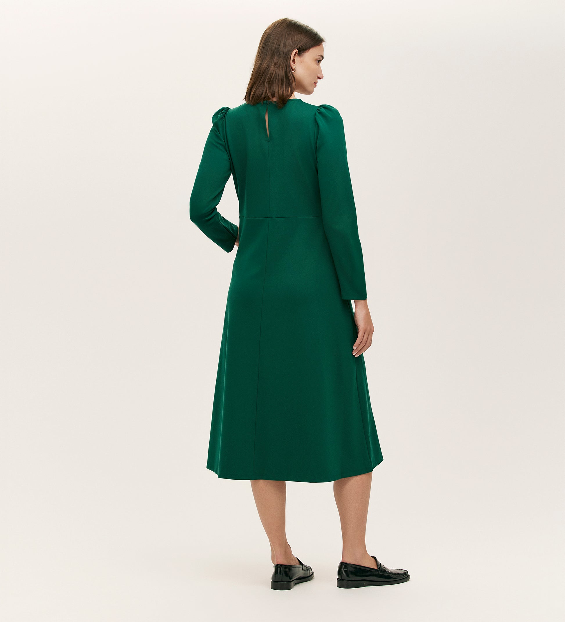 A woman faces away, wearing the Felice Bottle Green Ponte Jersey Midi Dress with black loafers, set against a plain light background.