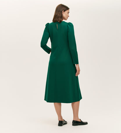 A woman faces away, wearing the Felice Bottle Green Ponte Jersey Midi Dress with black loafers, set against a plain light background.