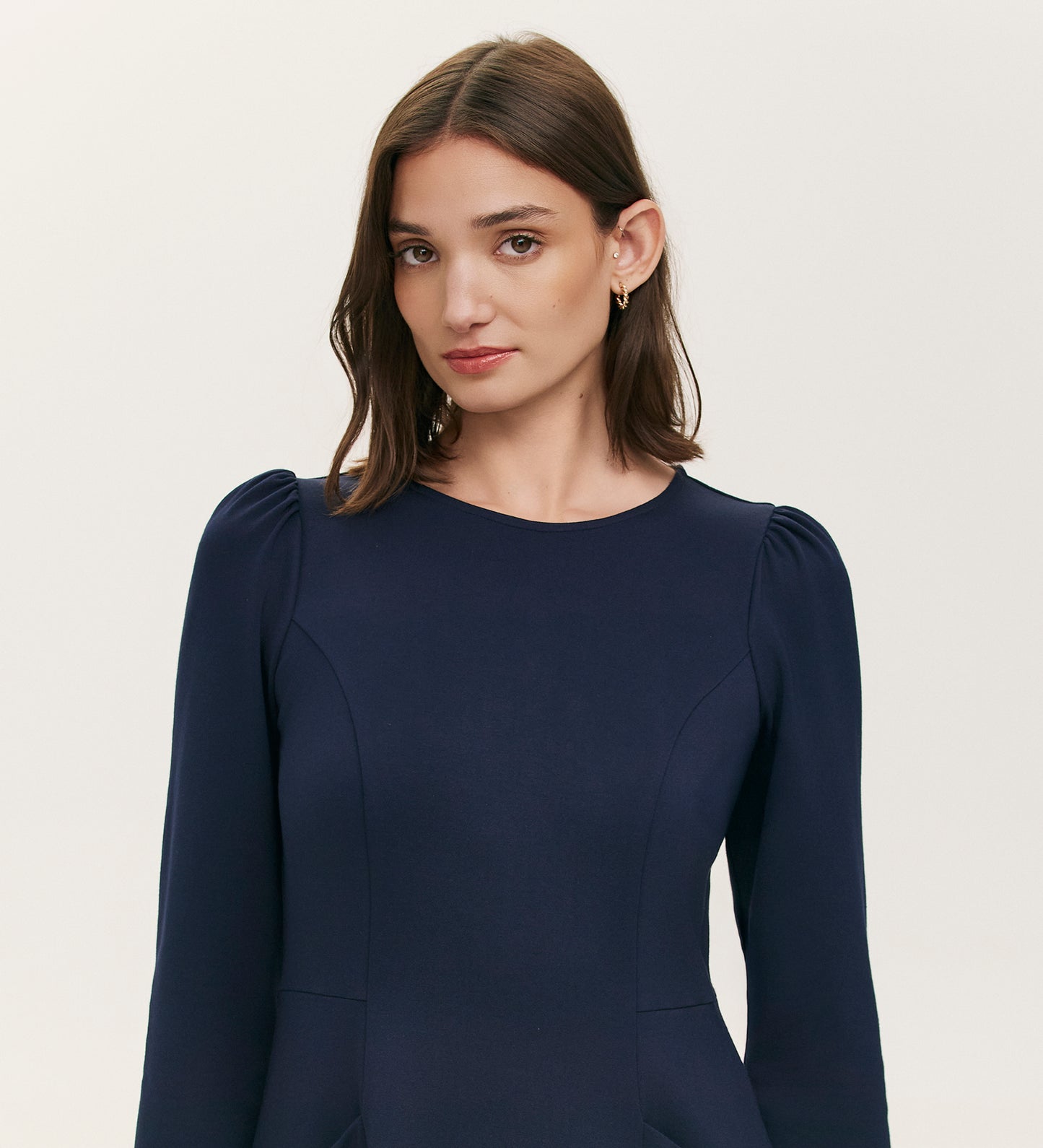 A woman with straight brown hair models the Felice Navy Ponte Jersey Midi Dress, featuring long sleeves, slight shoulder gathers, and a tailored silhouette, against a plain light background.