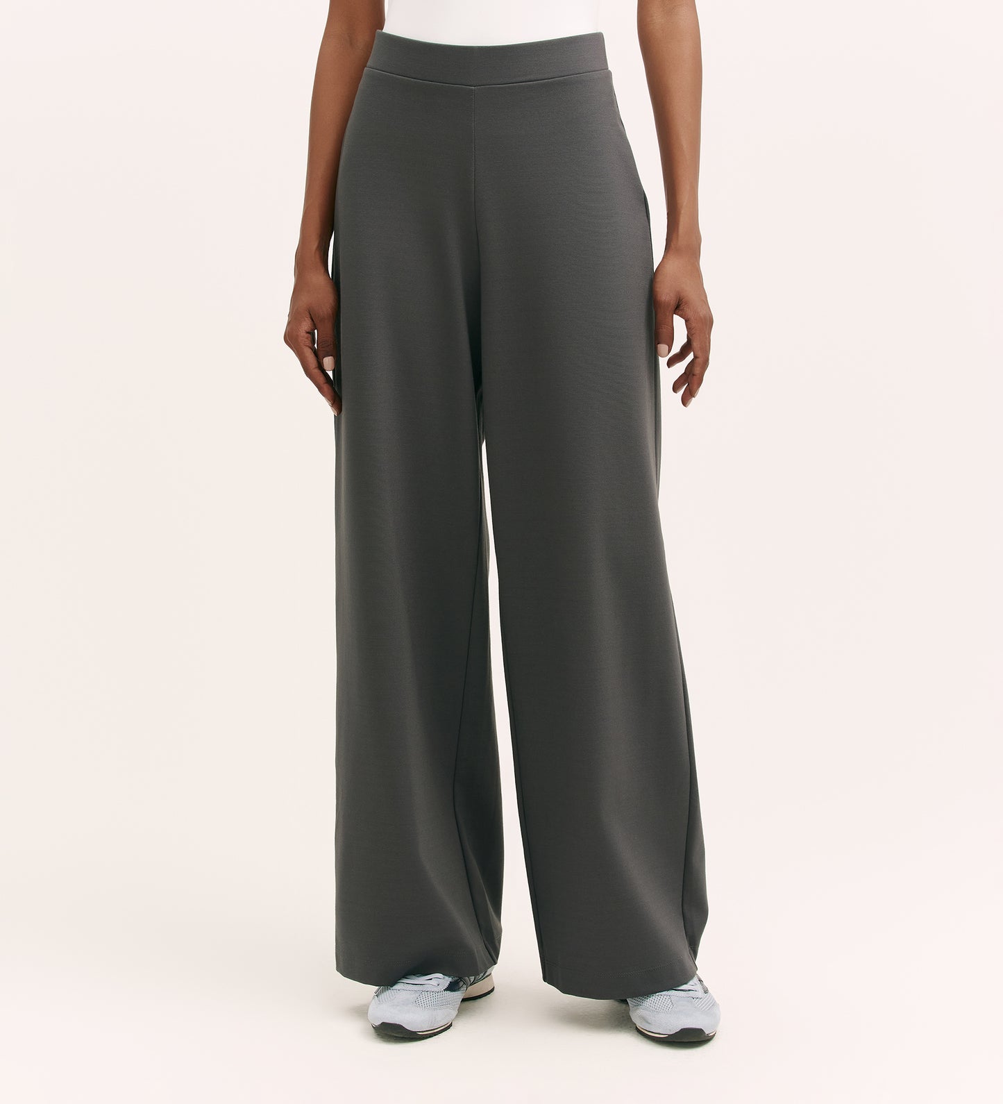 A person wears Kenzie Charcoal Ponte Jersey Wide Leg Trousers with an elasticated waistband and light sneakers, shown from the waist down against a plain, light background.