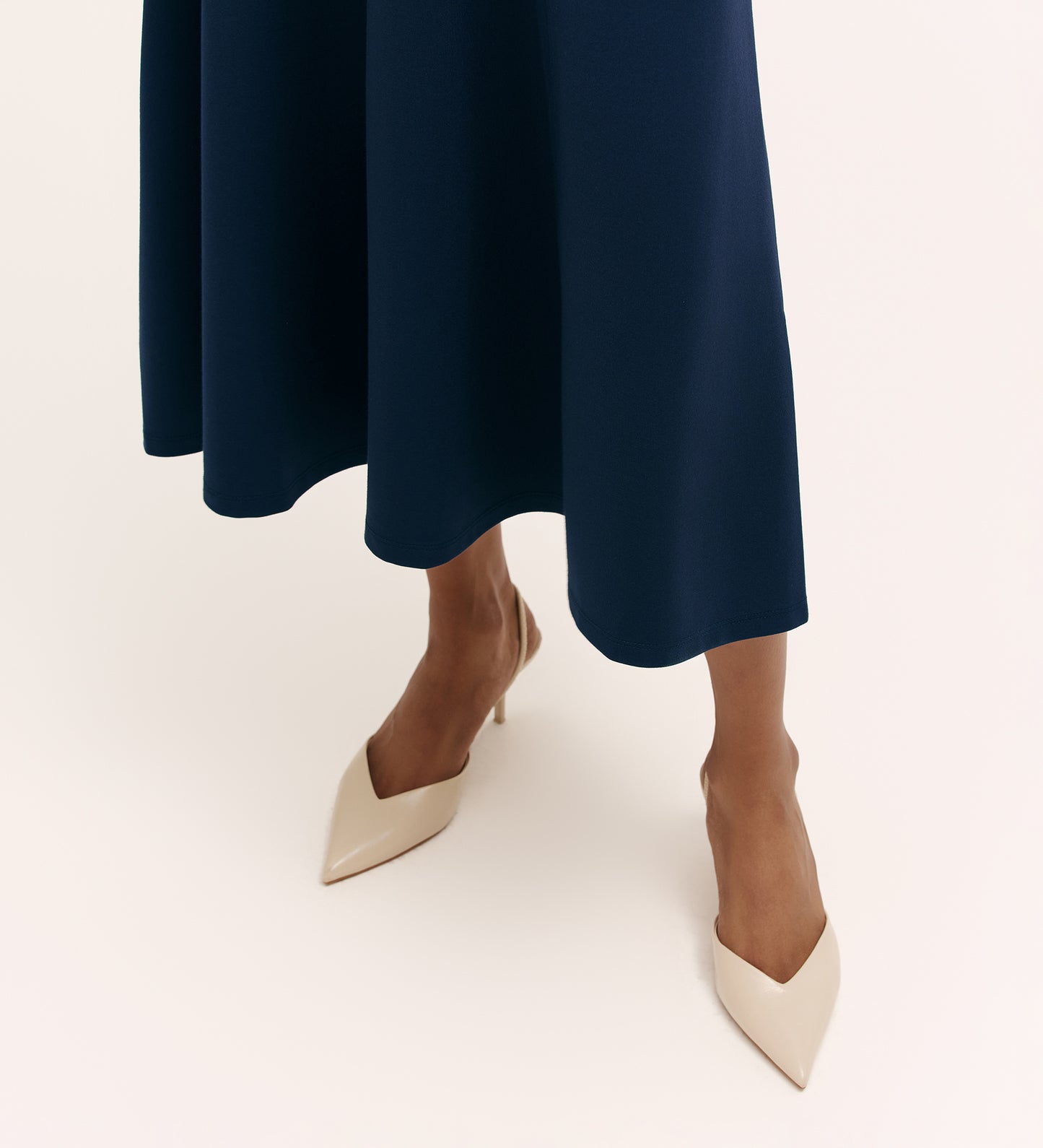 A person wears the Mae Navy Ponte Jersey Midi Skirt and pointed-toe beige heels, standing on a light background. The photo is cropped to display only the legs and shoes.
