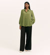 A woman with long dark hair poses confidently in the Melina Green Spot Chiffon Blouse, featuring a green polka dot pattern and lightweight fabric, styled with loose black pants and cream heels against a plain background.