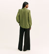 A woman stands facing away, wearing the Melina Green Spot Chiffon Blouse with black wide-leg pants against a plain light background.