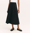 A person in a white sleeveless top and the Ruth Black Ponte Jersey Midi Skirt with an elasticated waistband, paired with black woven flats, stands against a plain light background.