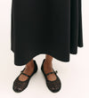 A person wearing the Ruth Black Ponte Jersey Midi Skirt with an elasticated waistband and black woven Mary Jane flats with a small buckle stands on a light background.