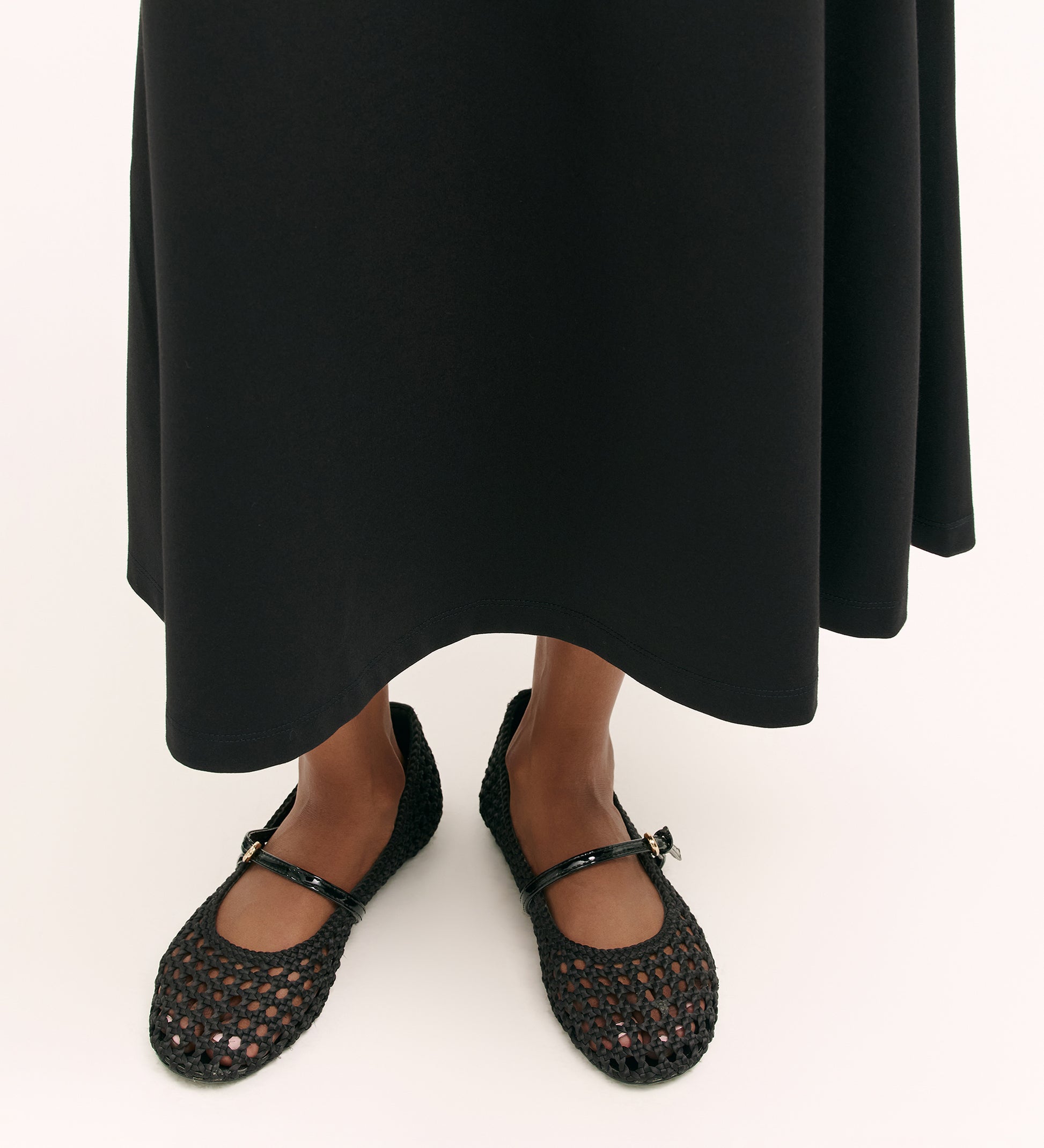 A person wearing the Ruth Black Ponte Jersey Midi Skirt with an elasticated waistband and black woven Mary Jane flats with a small buckle stands on a light background.