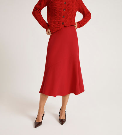 A person wears the Gracie Red Rich Crepe Midi Skirt and a matching red cardigan with a flared silhouette, paired with pointed brown heels, hands on hips, against a white background.