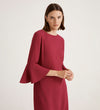 A woman with straight brown hair wears the Izzy Berry Crepe Short Dress, featuring dramatic bell sleeves, standing against a light background and looking slightly to the side with a neutral expression.