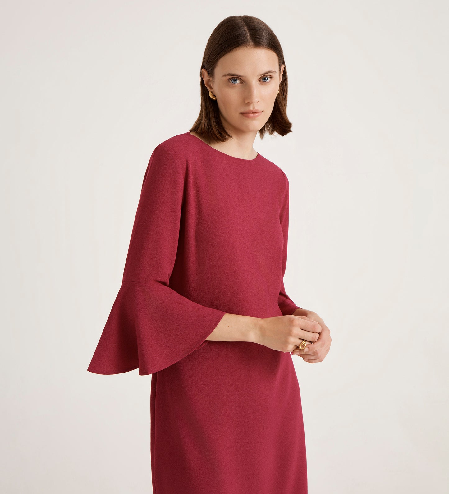 A woman with straight brown hair wears the Izzy Berry Crepe Short Dress, featuring dramatic bell sleeves, standing against a light background and looking slightly to the side with a neutral expression.