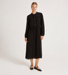 A woman stands against a plain background wearing the Jasmine Black Lace Trim Crepe Midi Dress with long sleeves and button details. She pairs it with black flats, her hair pulled back, and her arms relaxed by her sides.