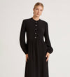 A woman stands calmly against a plain light background, wearing the Jasmine Black Lace Trim Crepe Midi Dress with a vintage-inspired silhouette and looking at the camera.