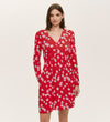 A woman in the Joanne Red Poppies Jersey Short Dress, featuring long sleeves, a V-neckline, and a white floral print, stands against a plain light background, embodying effortless everyday comfort.