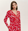 A woman with straight brown hair confidently models the Joanne Red Poppies Jersey Short Dress, featuring long sleeves and a red floral print, standing against a plain light background and showcasing comfortable, everyday style.