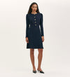 A woman faces forward in the Kadie Navy Crepe Short Dress, featuring long sleeves, a fitted waist, gold front buttons, and black pointed-toe heels, set against a plain light background.