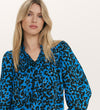 A woman with long blonde hair wears the Kiya Blue Animal Crepe Long Sleeve Blouse, featuring a relaxed fit and neckline frills, standing against a plain light background.