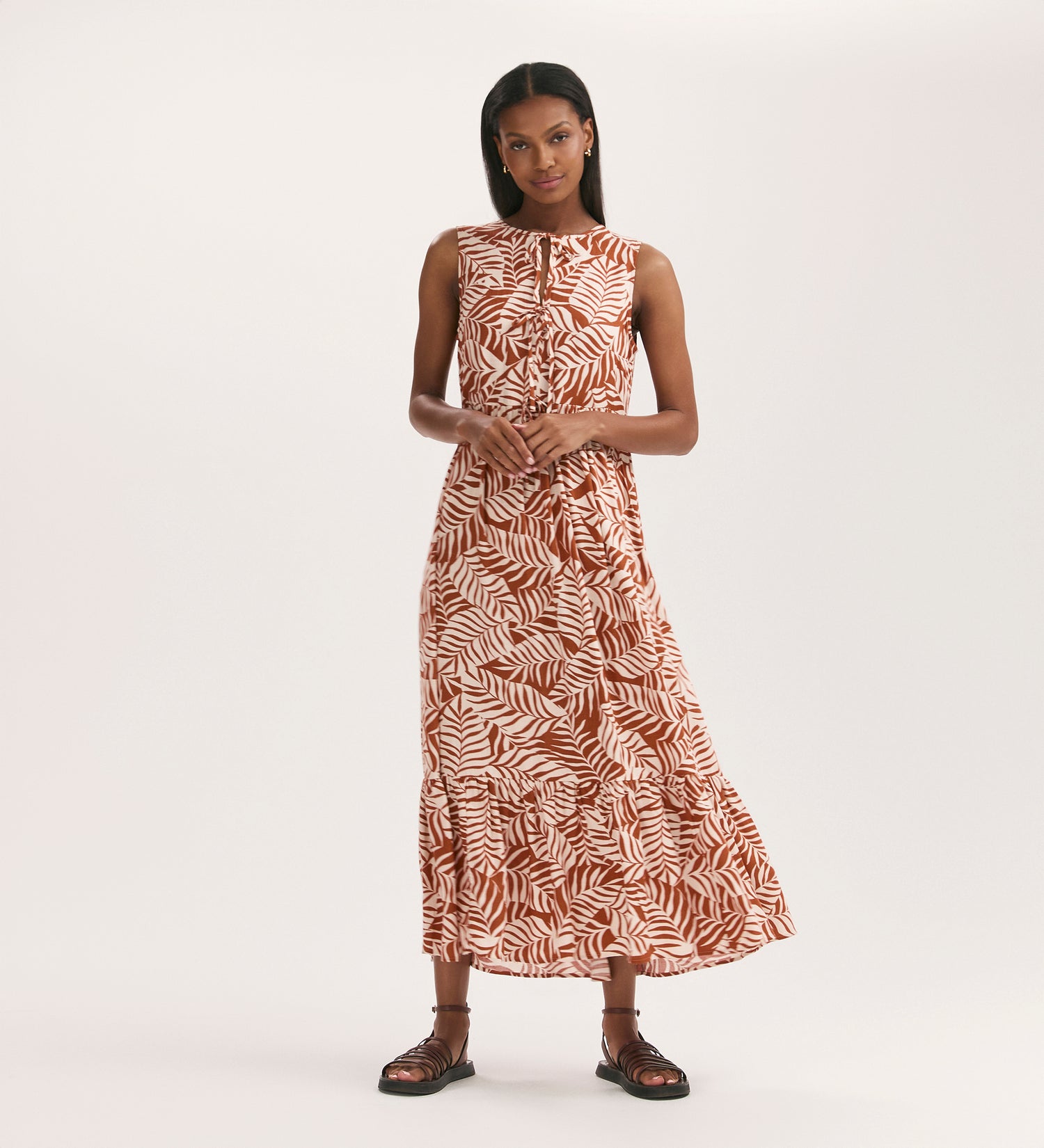 A woman with straight dark hair stands against a plain background wearing the Larissa Tan Leaf Tie Front Midi Dress with functional pockets and black sandals, her hands gently clasped in front of her.