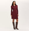 A woman stands against a plain light background wearing the Lea Burgundy Ponte Jersey Short Dress with a collared neckline and zipper, paired with tall dark brown heeled boots.
