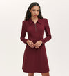 A woman with long curly hair models the Lea Burgundy Ponte Jersey Short Dress, which features a collared neckline and front zipper, standing against a plain light background.