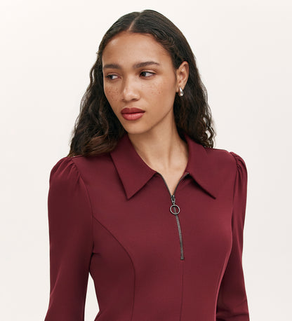 A woman with long, wavy brown hair and freckles wears the Lea Burgundy Ponte Jersey Short Dress with a collared neckline and zippered front, looking to the side against a plain light background.